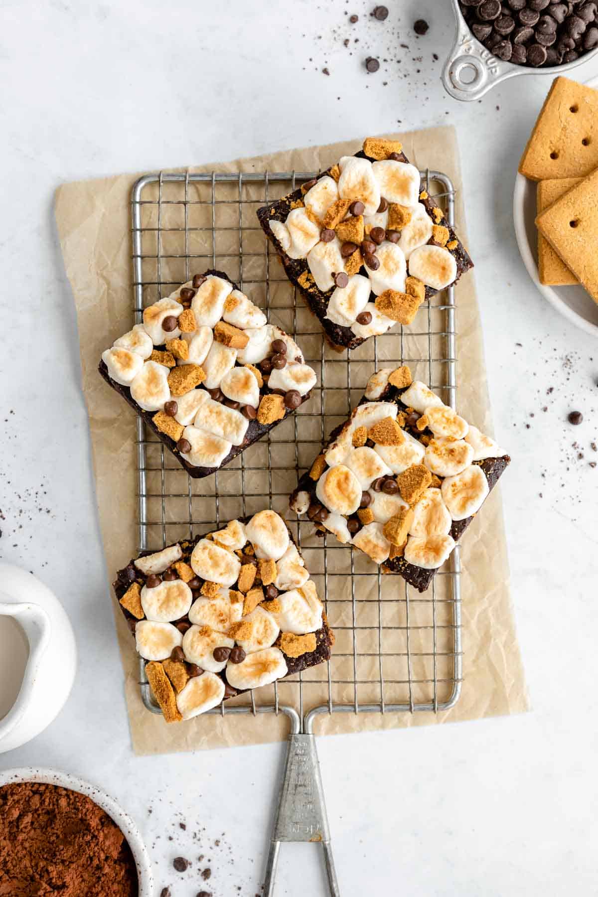 vegan s'mores brownies on a wire cooling rack beside a bowl of graham crackers, chocolate chips, and cocoa