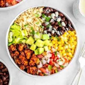 a vegan tempeh burrito bowl with black beans, corn, avocado, lettuce, and pico de gallo