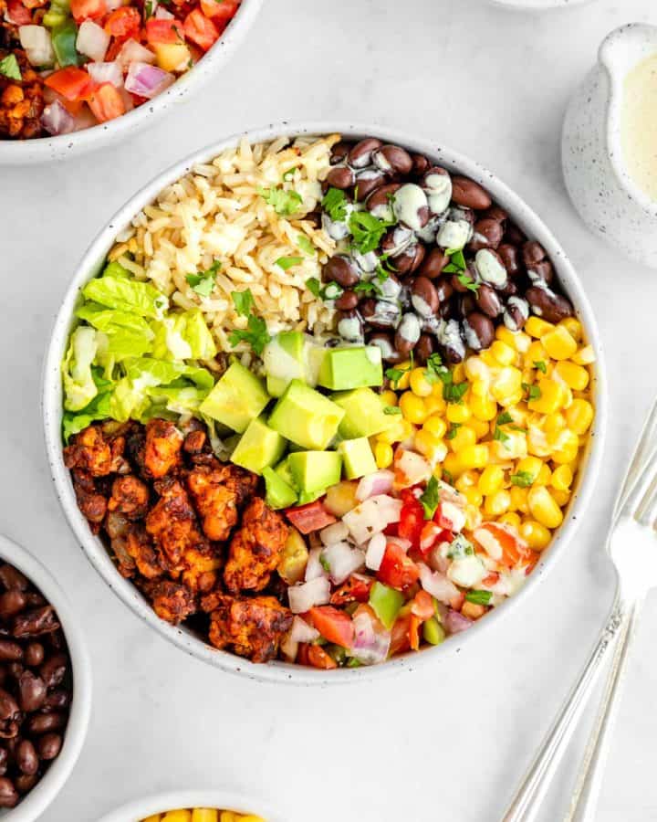 a vegan tempeh burrito bowl with black beans, corn, avocado, lettuce, and pico de gallo