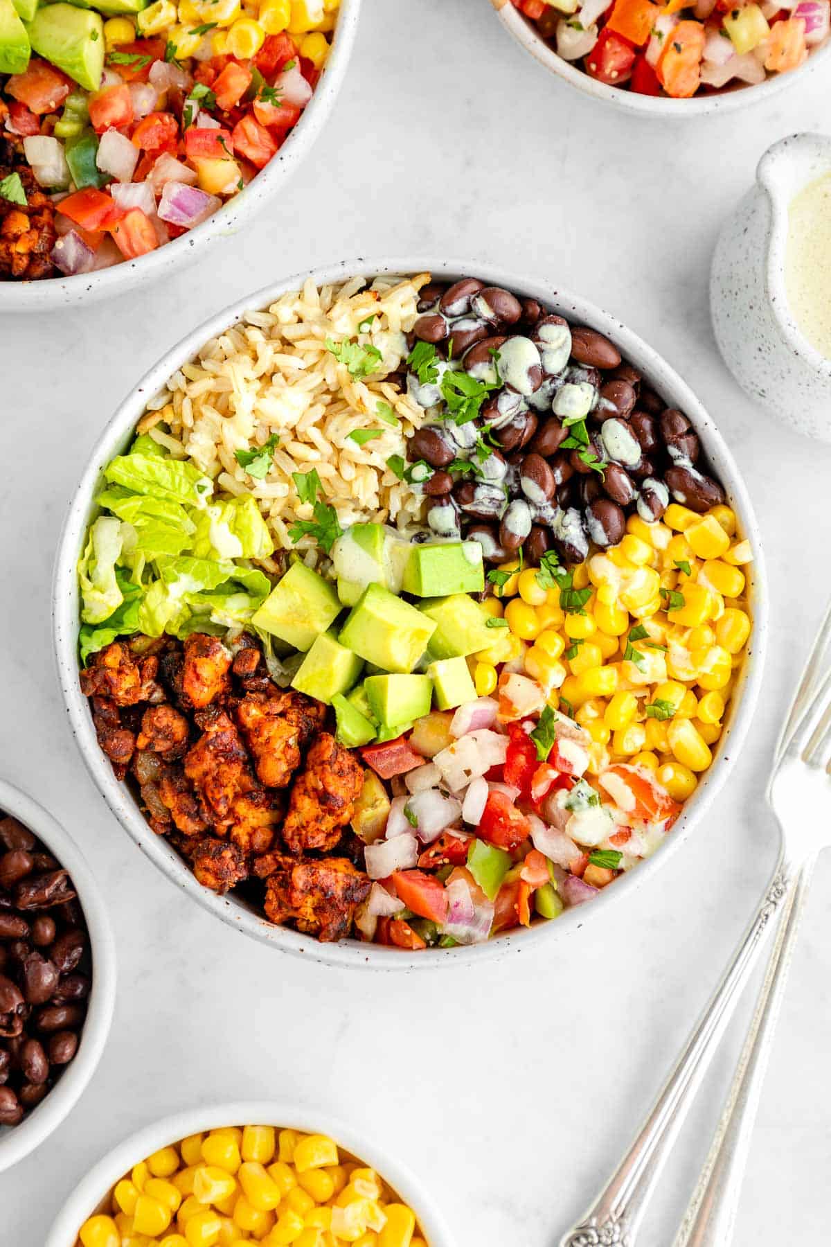 a vegan tempeh burrito bowl with black beans, corn, avocado, lettuce, and pico de gallo