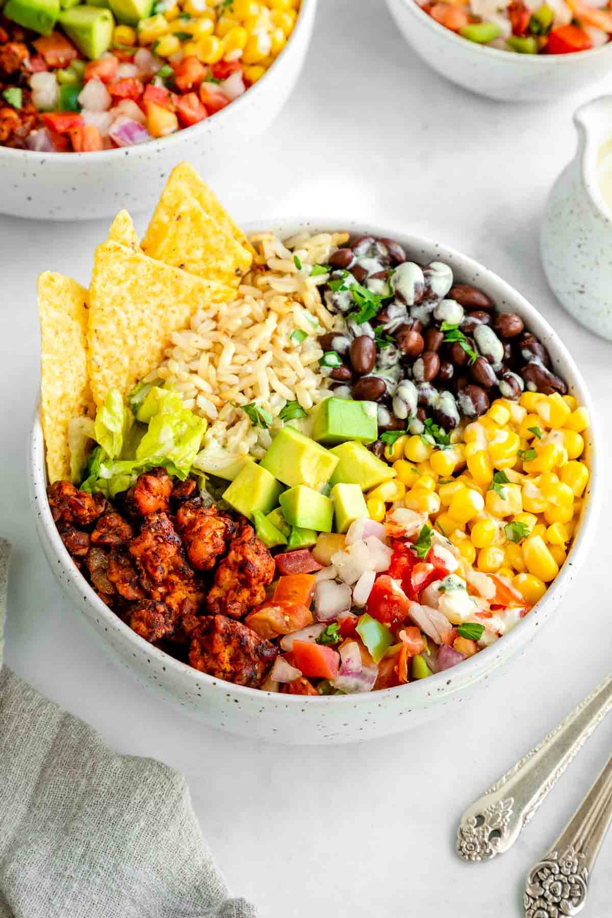 a vegan tempeh burrito bowl with corn tortilla chips on top