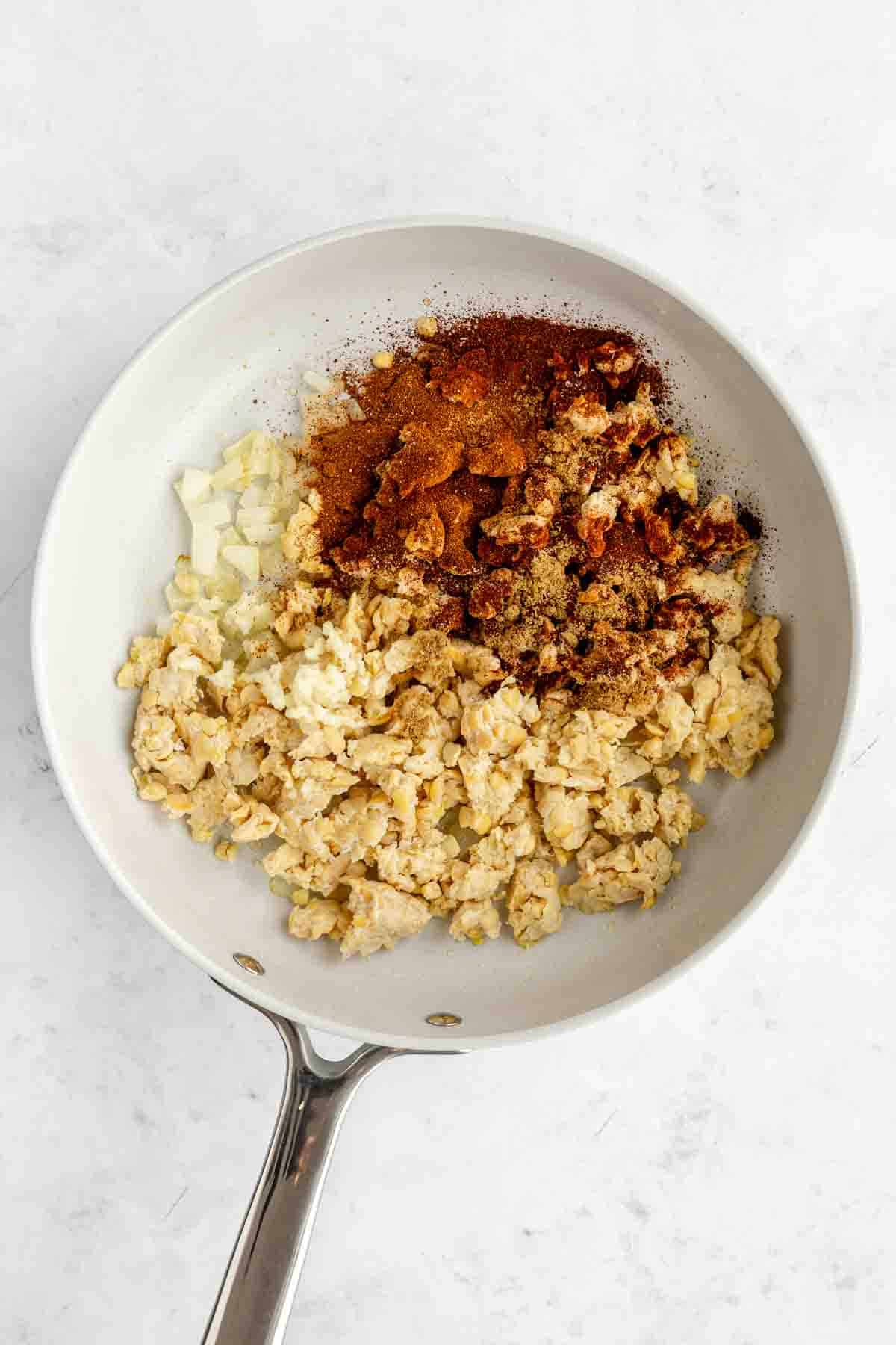 crumbled tempeh, diced onion, and spices in a ceramic frying pan
