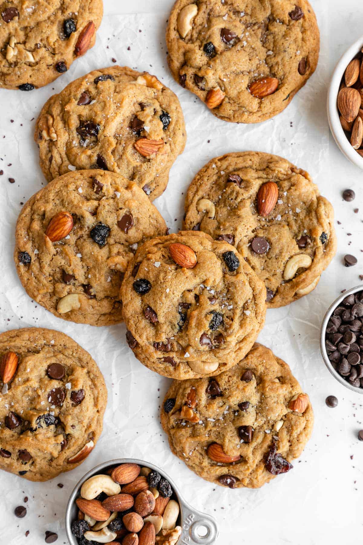 a pile of vegan trail mix cookies beside a bowl of mixed nuts and fruit