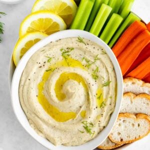 white bean dip in a white bowl with carrots, celery, bread, and lemon