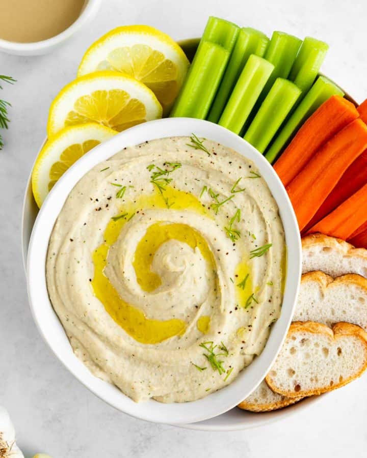 white bean dip in a white bowl with carrots, celery, bread, and lemon