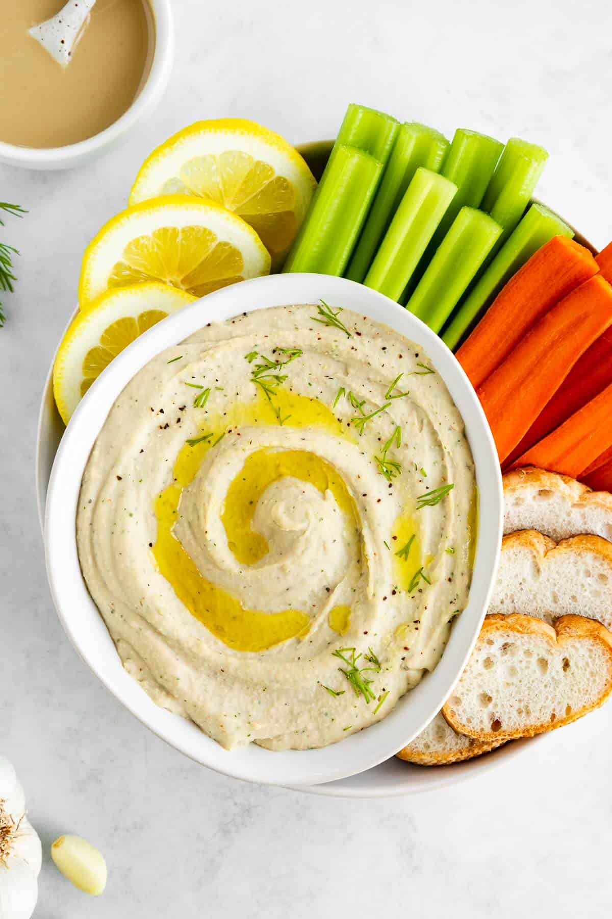 white bean dip in a white bowl with carrots, celery, bread, and lemon