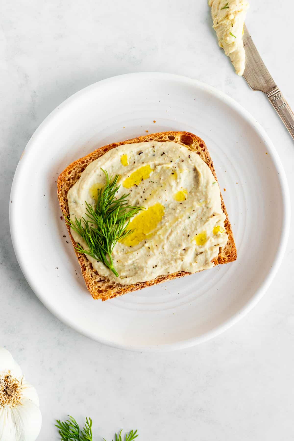 white bean hummus spread on a piece of toast on a white plate