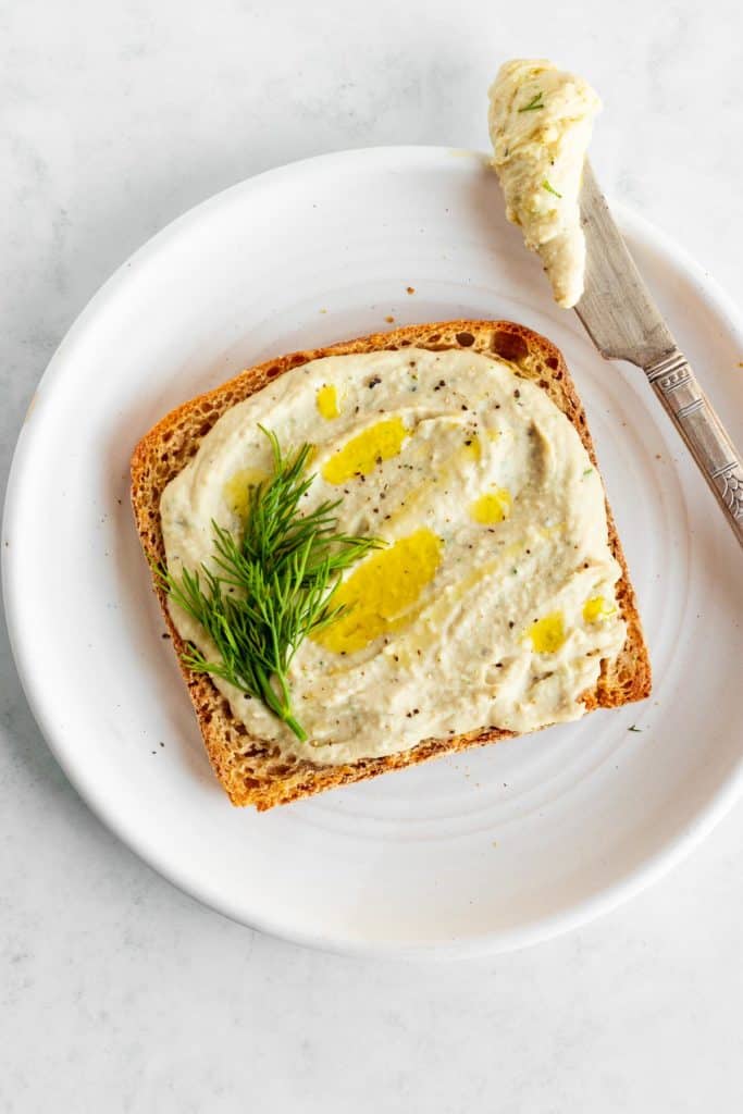 white bean hummus spread on a piece of toast on a white plate