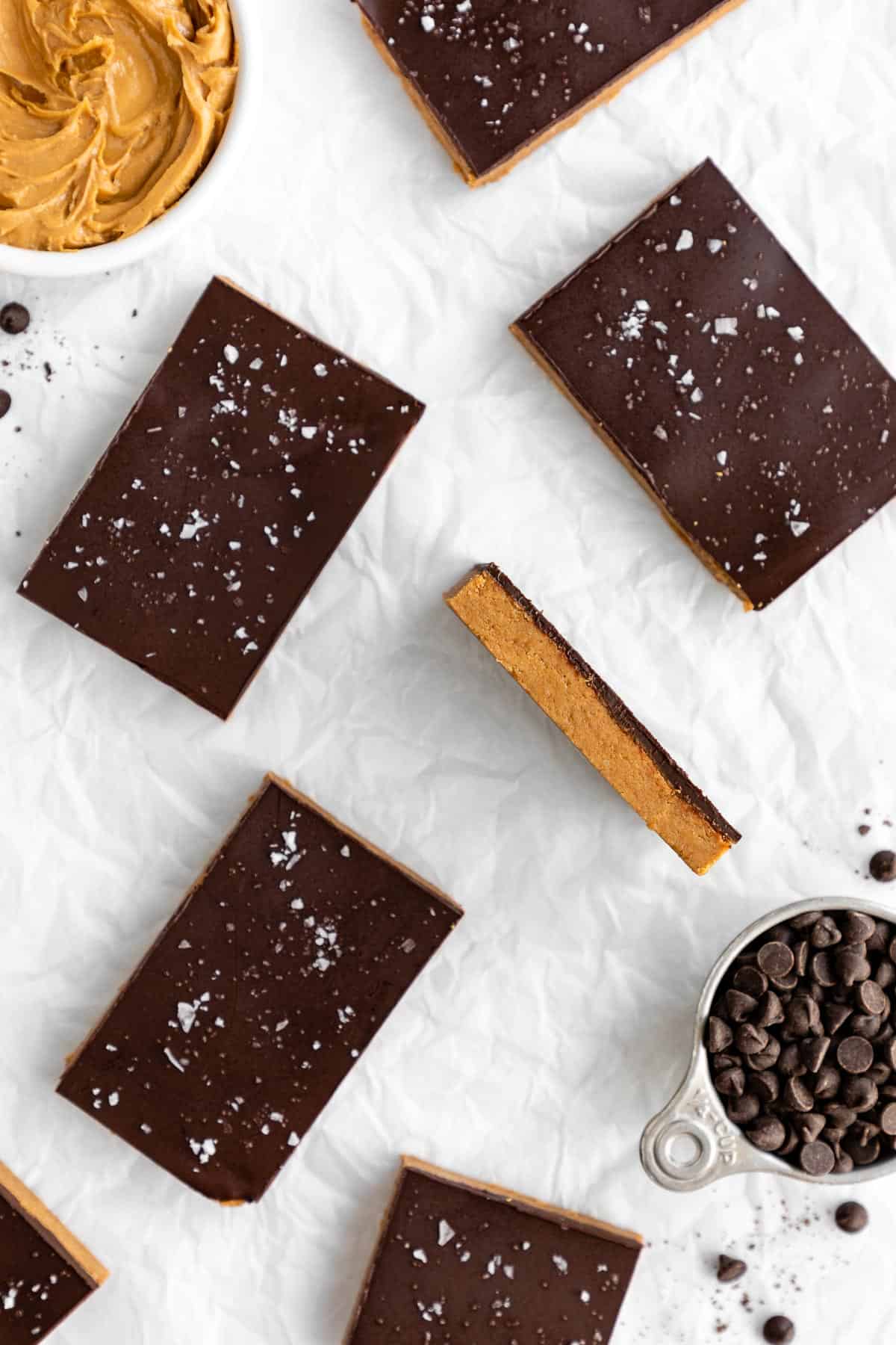 homemade chocolate peanut butter protein bars on white parchment paper beside a measuring cup filled with chocolate chips