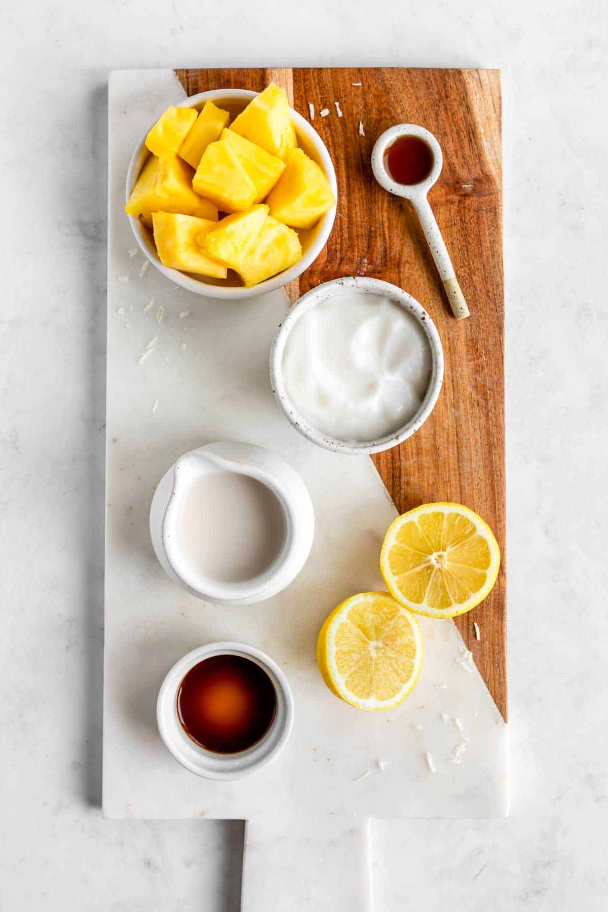 pineapple, coconut yogurt, coconut milk, maple syrup, lemons, and vanilla extract on a marble serving board