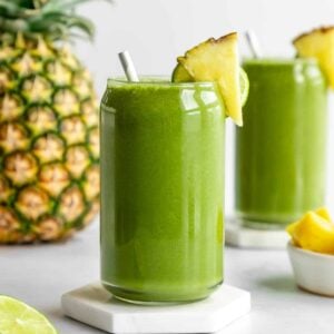 pineapple green smoothie inside two glasses beside a large pineapple