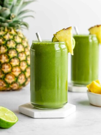 pineapple green smoothie inside two glasses beside a large pineapple