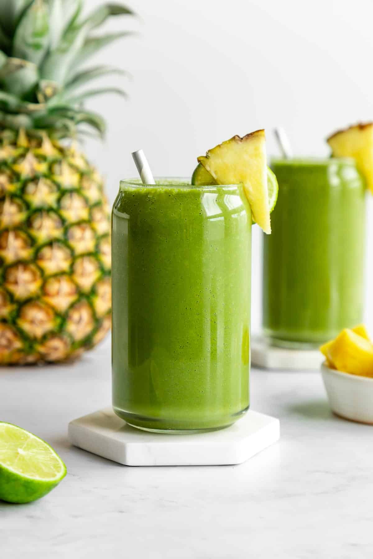 pineapple green smoothie inside two glasses beside a large pineapple