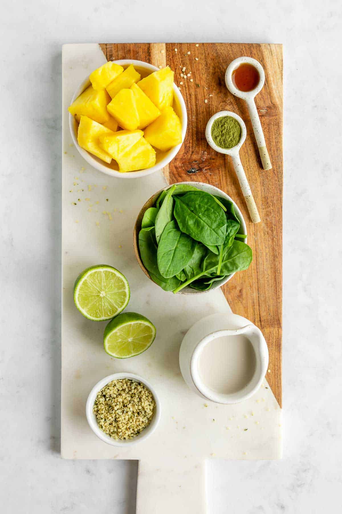 a marble serving board topped with pineapple, spinach, lime, hemp seeds, and almond milk