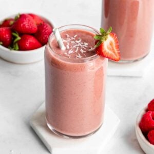 a strawberry banana smoothie inside a glass beside a bowl of berries