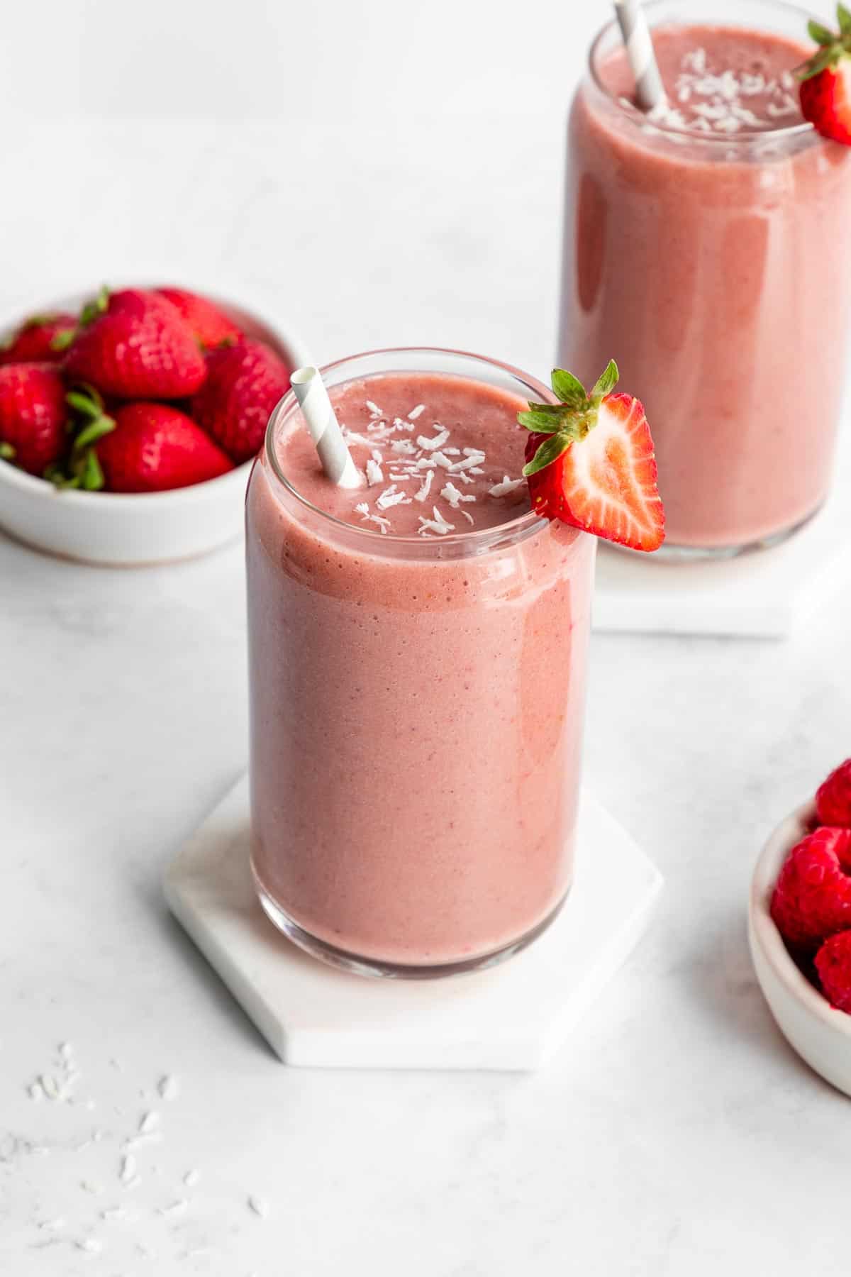 a strawberry banana smoothie inside a glass beside a bowl of berries
