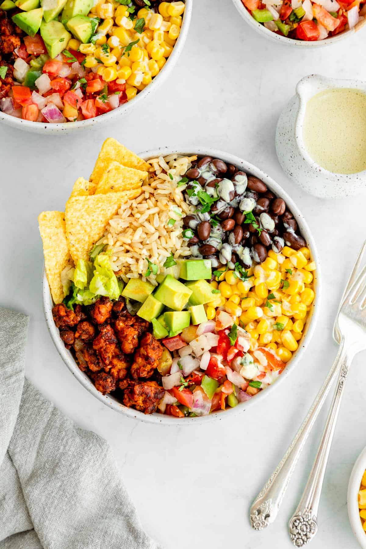 a vegan tempeh bowl with black beans, rice, corn, tomatoes, and corn tortilla strips