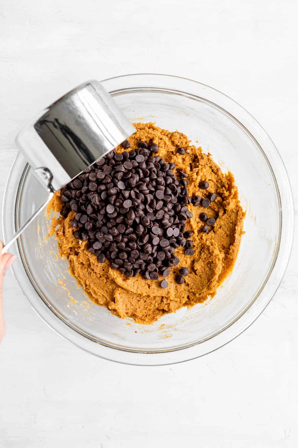 a measuring cup pouring chocolate chips in vegan pumpkin cookie dough