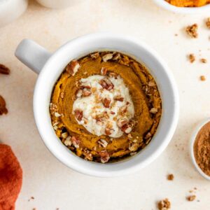 vegan pumpkin mug cake inside a white mug with frosting and pecans on top