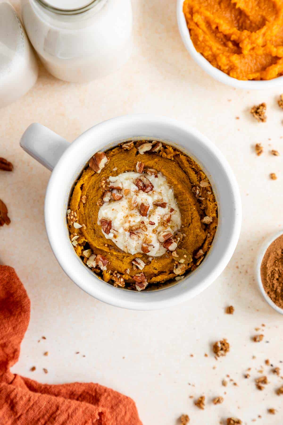 vegan pumpkin mug cake inside a white mug with frosting and pecans on top