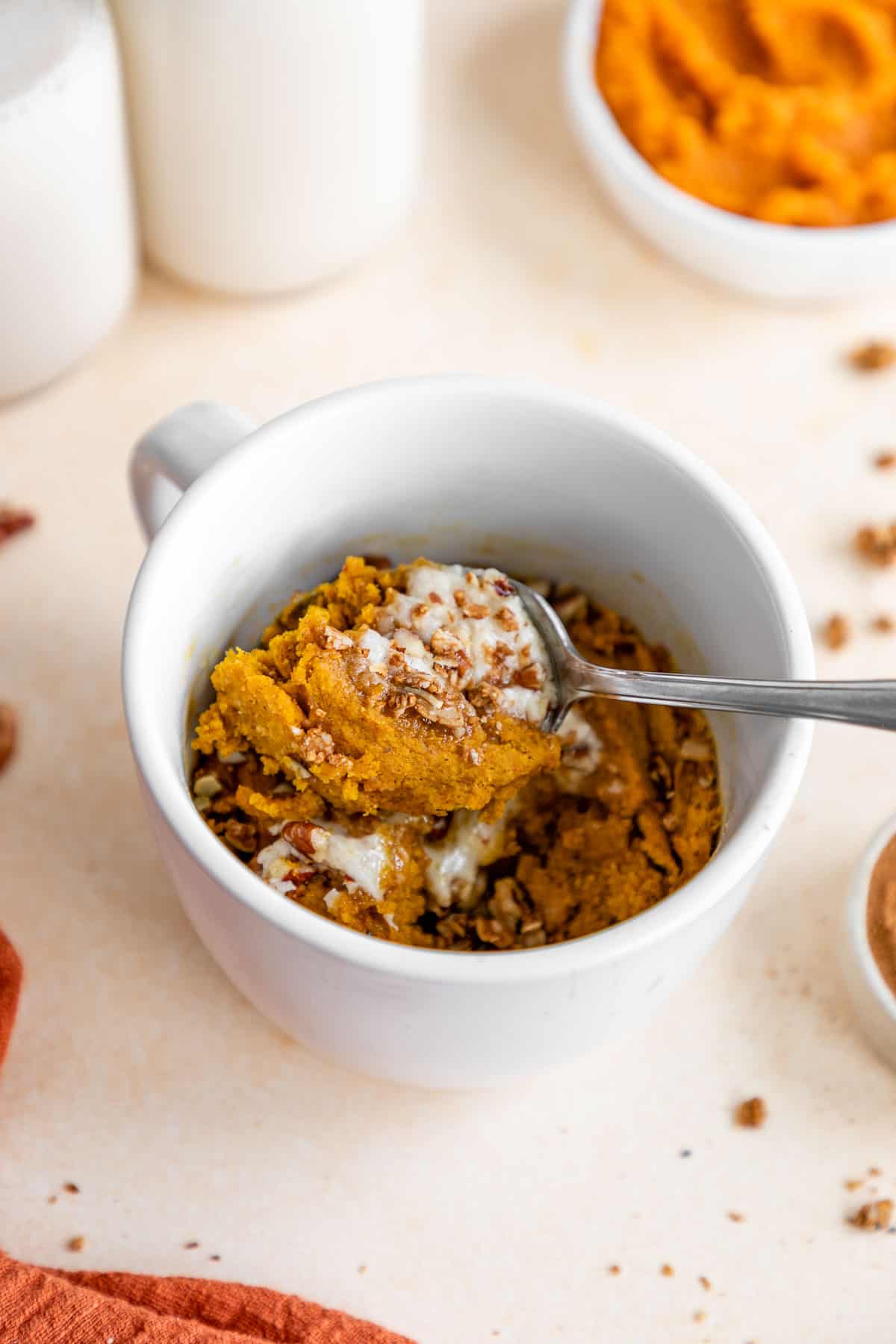 a spoon scooping a bite of vegan pumpkin mug cake out of a white mug