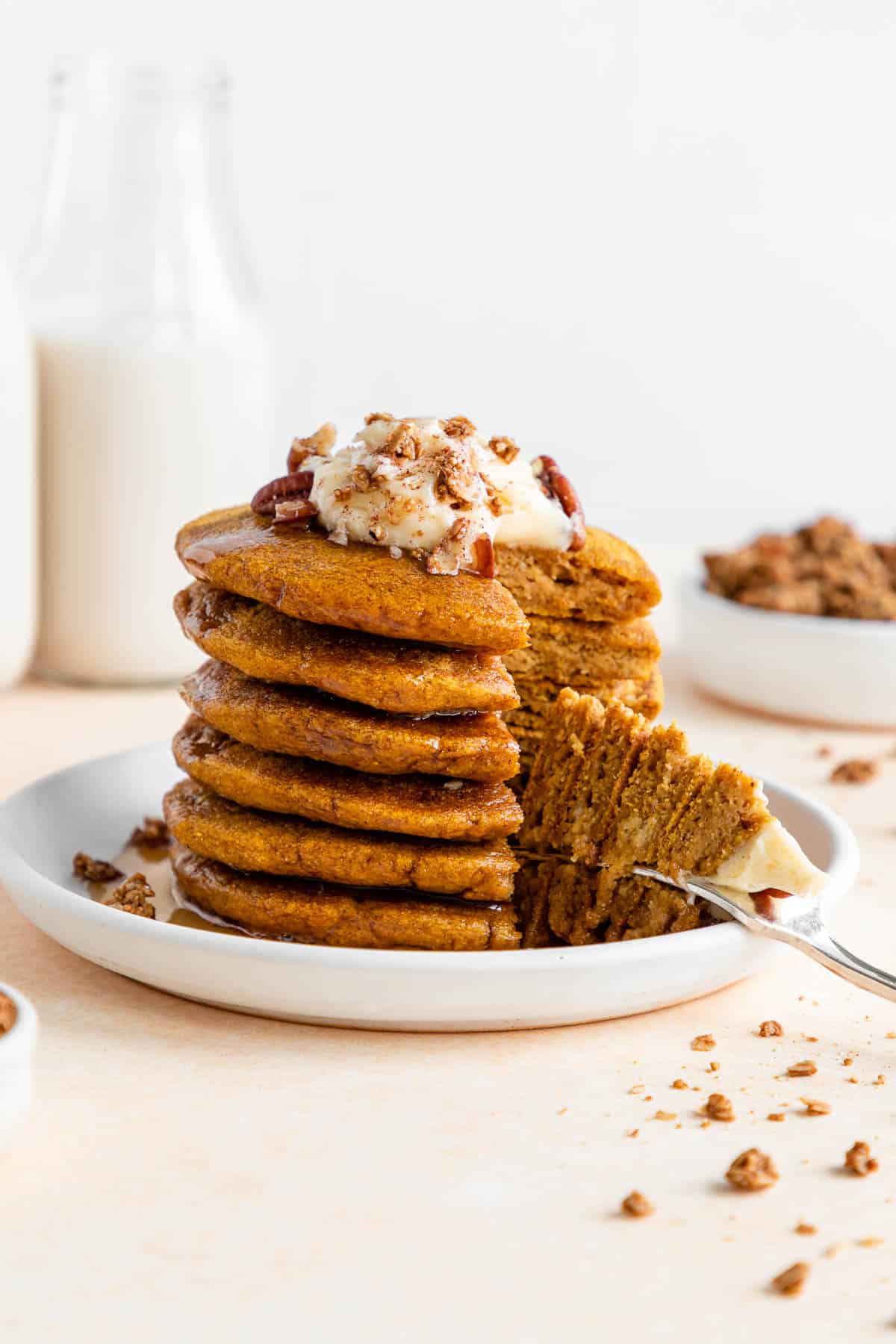 a fork digging into a stack of vegan pumpkin pancakes with maple syrup