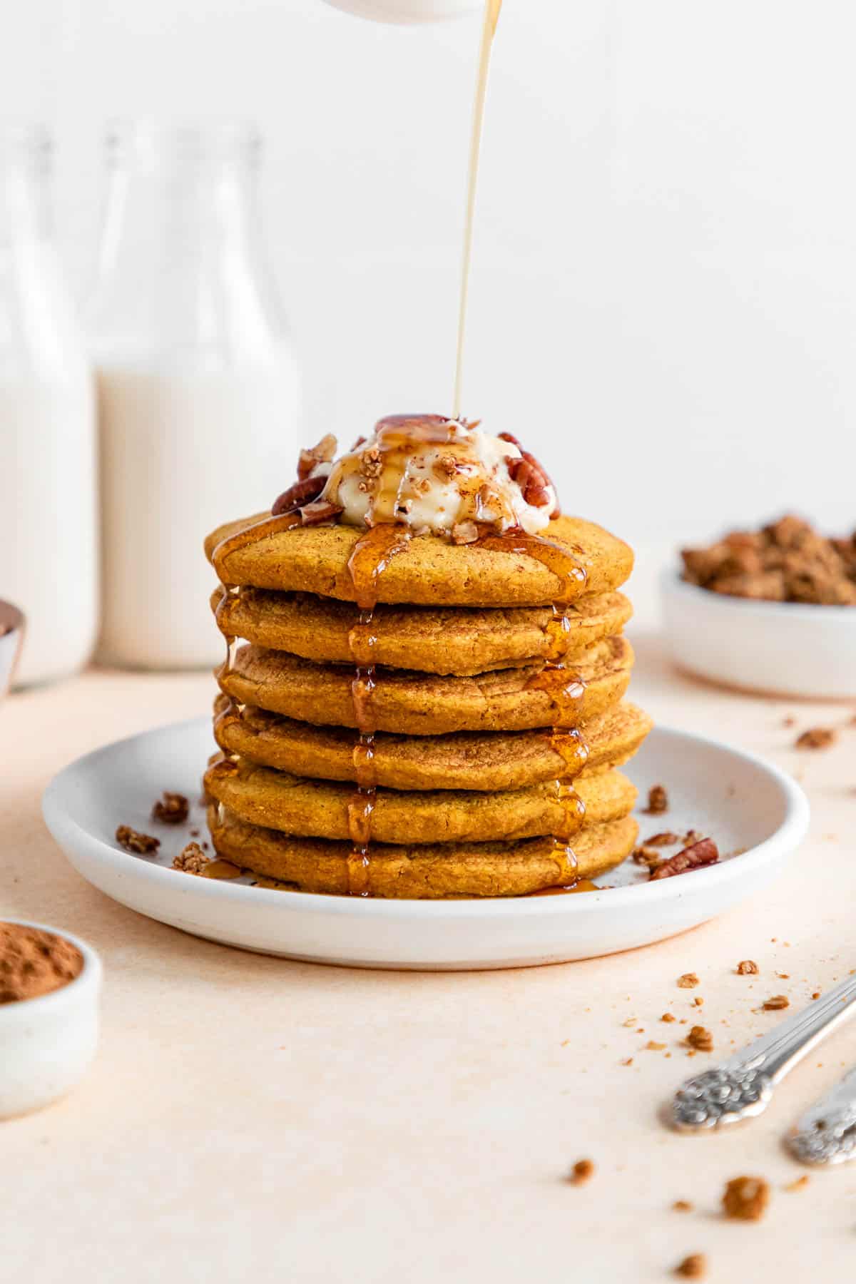 pouring maple syrup over a stack of vegan pumpkin pancakes on a plate