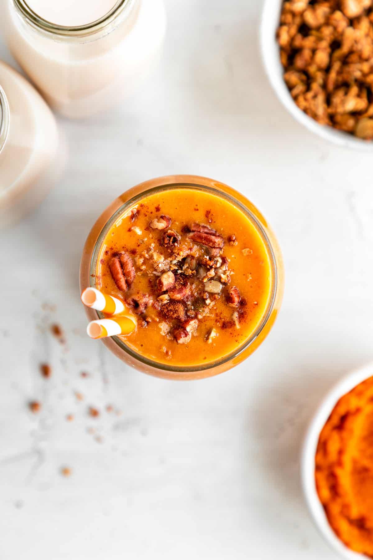 overhead image of a vegan pumpkin pie smoothie in a glass with granola and pecans on top