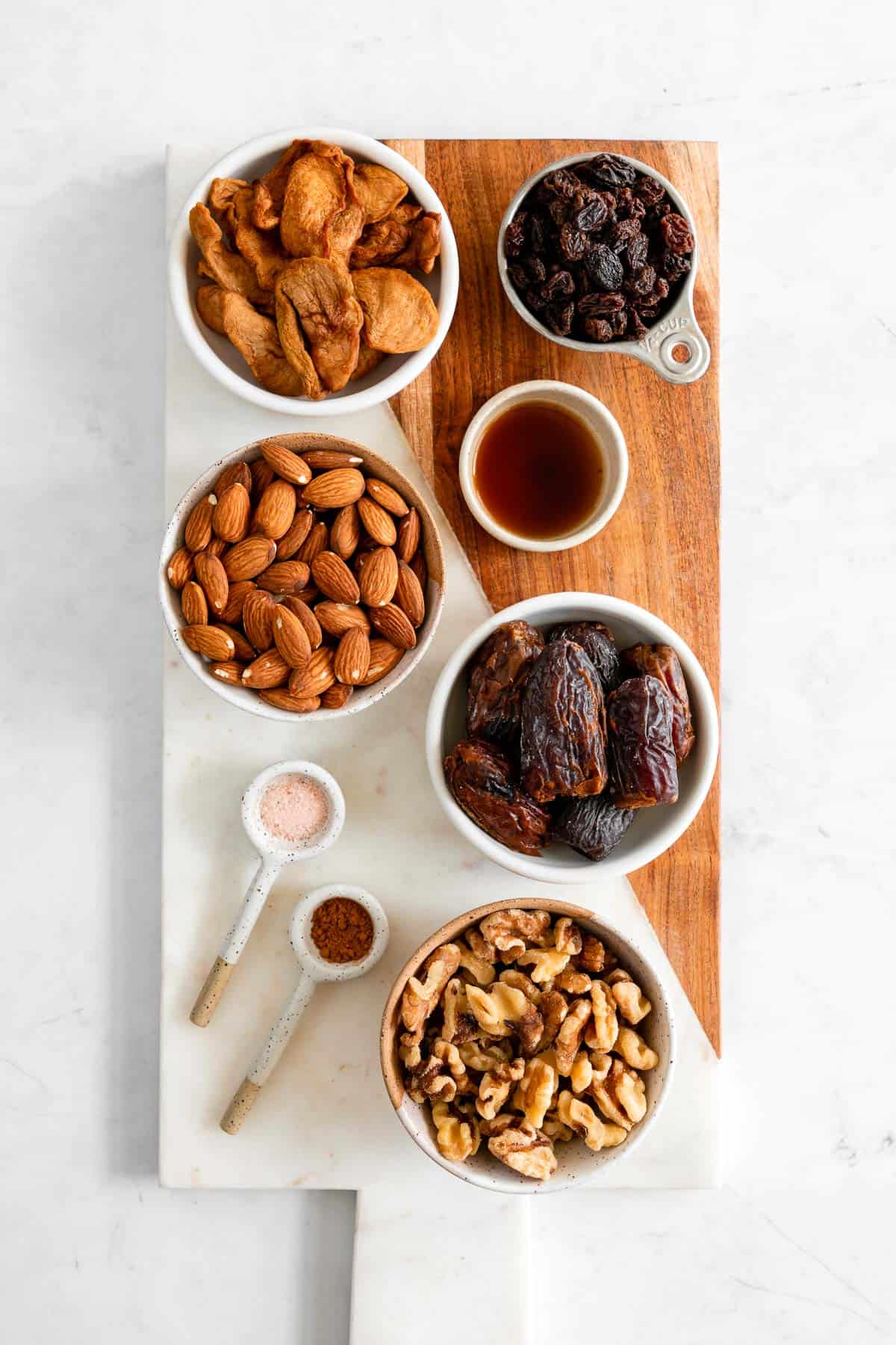 a serving board with bowls of almonds, walnuts, medjool dates, soft dried apples, raisins, cinnamon, vanilla, and salt