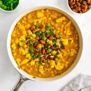 turmeric curry with chickpeas and cauliflower inside a skillet, topped with golden almonds and cilantro