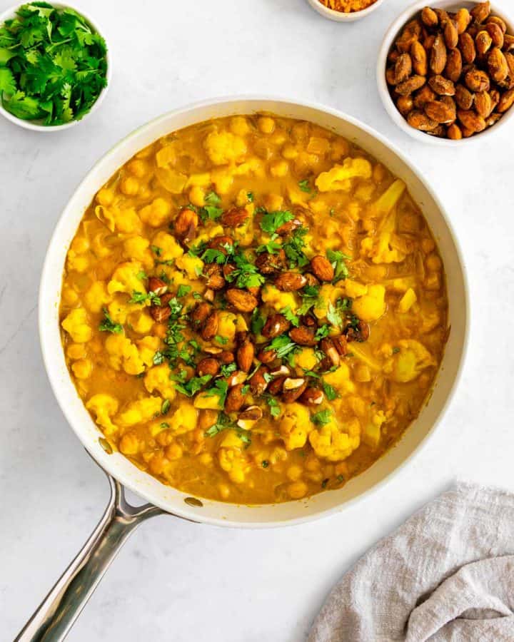 turmeric curry with chickpeas and cauliflower inside a skillet, topped with golden almonds and cilantro