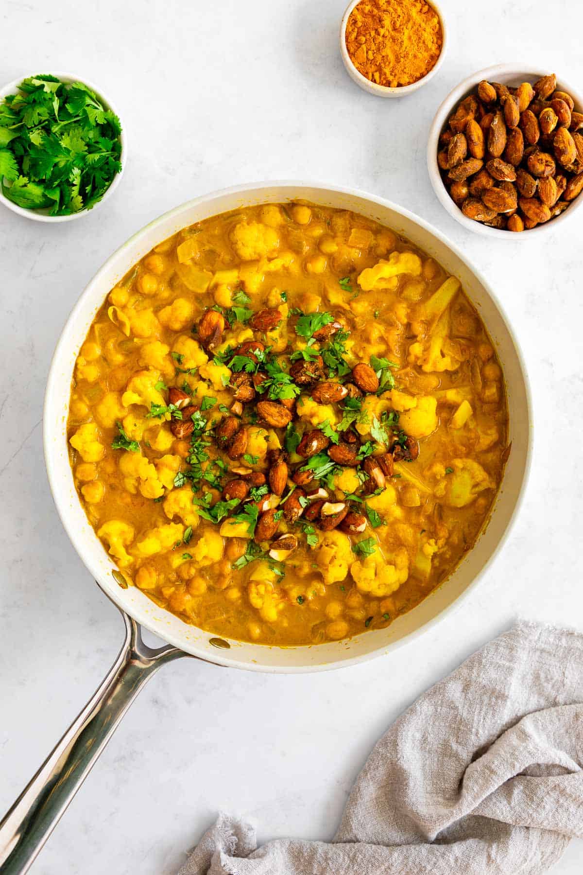 turmeric curry with chickpeas and cauliflower inside a skillet, topped with golden almonds and cilantro