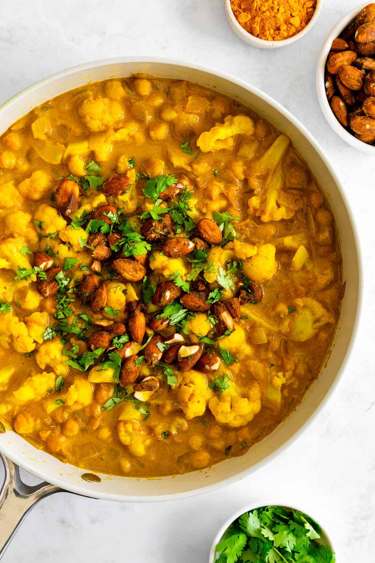 turmeric curry with chickpeas and cauliflower in a skillet, topped with chopped almonds and cilantro