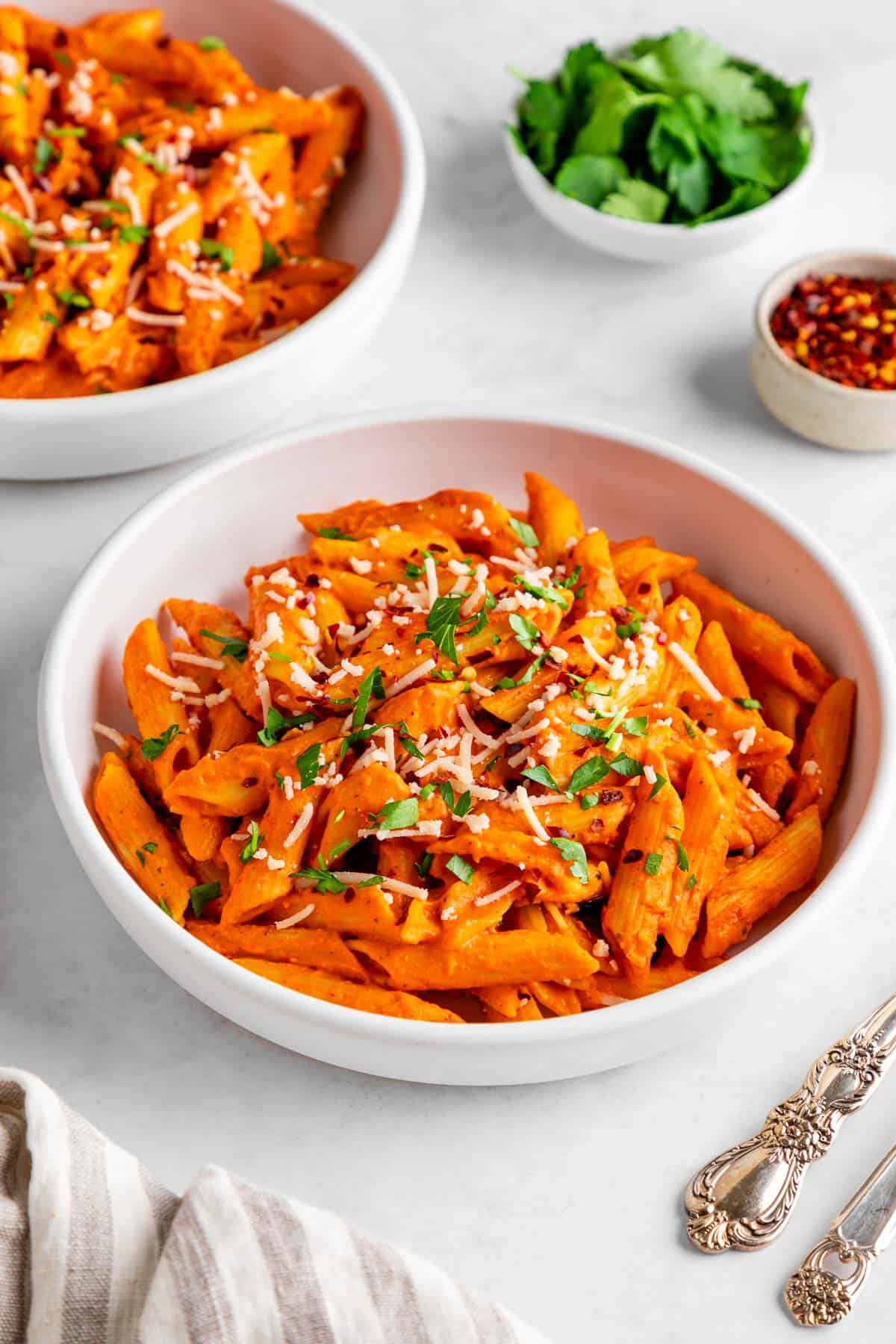 two bowls filled with vegan roasted red pepper pasta with vegan parmesan and fresh parsley