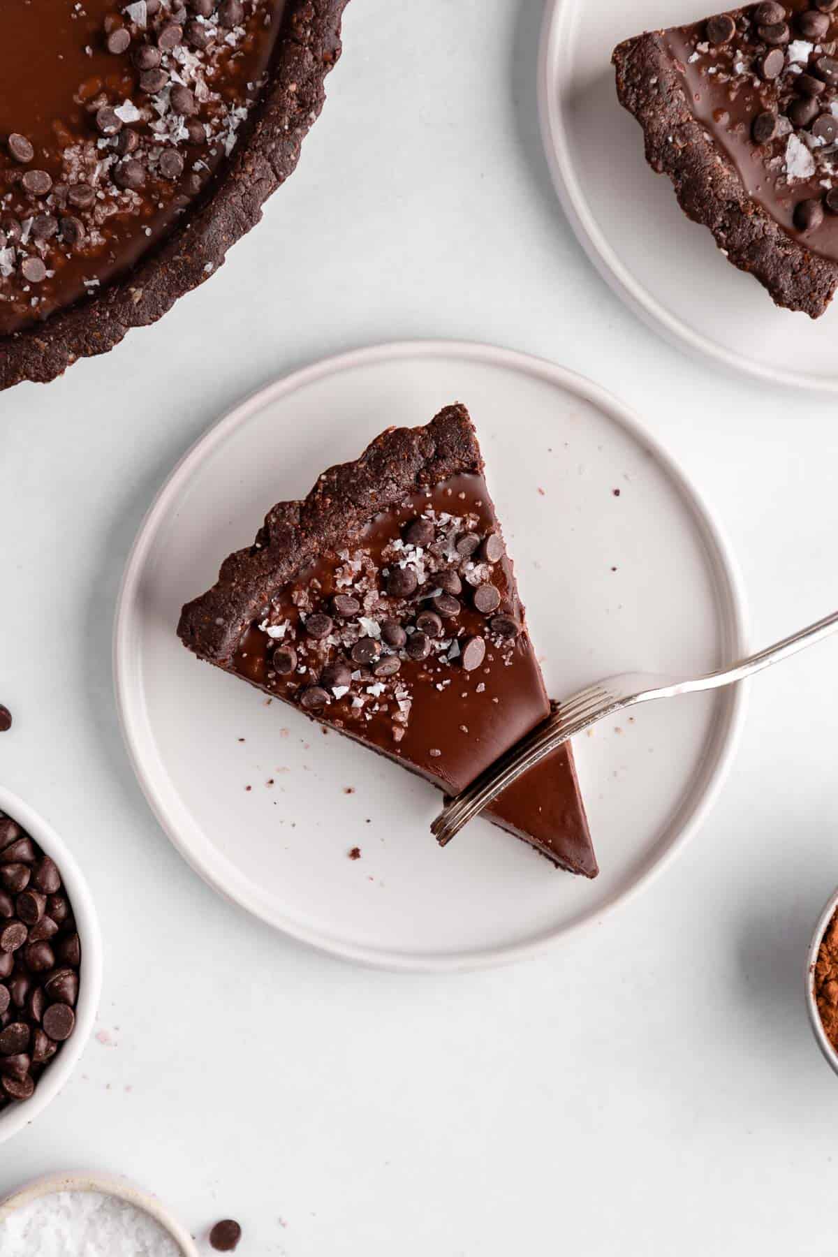 a fork slicing into a slice of no-bake vegan chocolate tart on a white plate