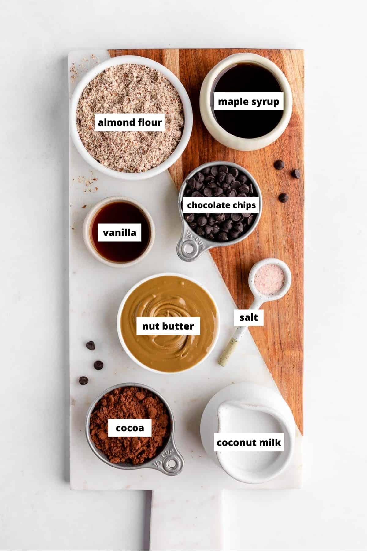 no-bake vegan chocolate tart ingredients on a marble board, including almond flour, nut butter, coconut milk, cocoa, and chocolate chips