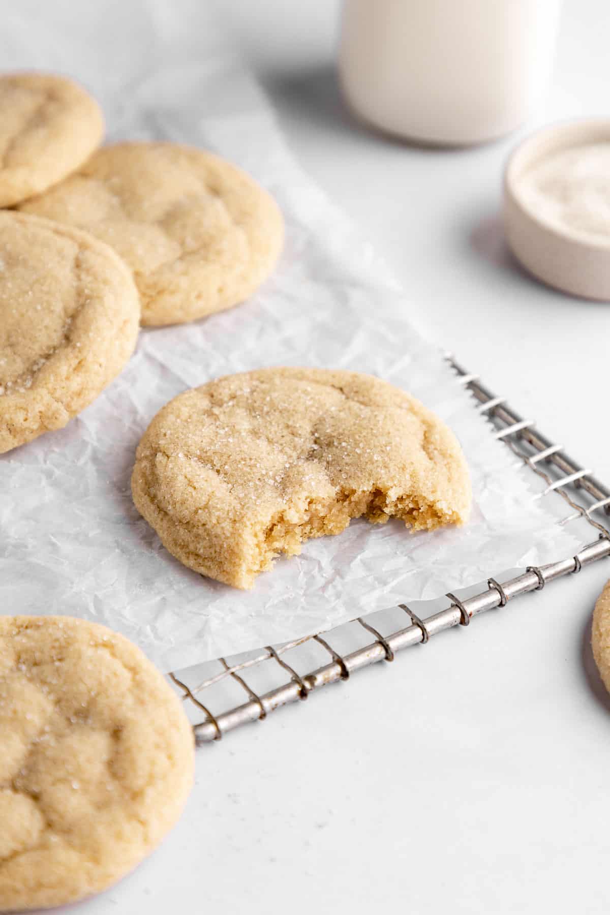 vegan sugar cookies on white parchment paper with a bite taken out of the center cookie