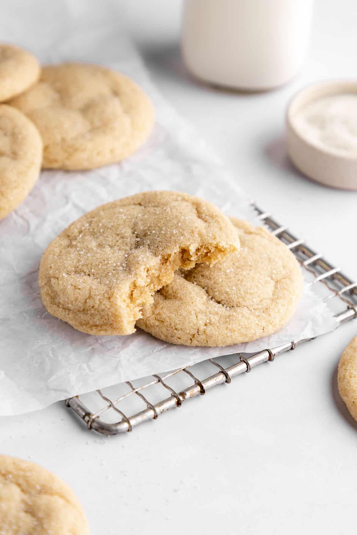 vegan sugar cookies on white parchment paper with a bite taken out of the center cookie