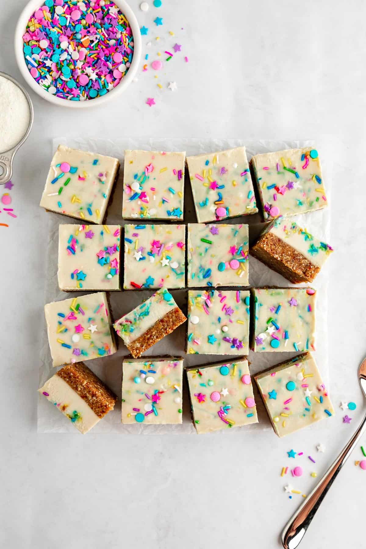 a pile of vegan no-bake funfetti cheesecake bars with rainbow sprinkles