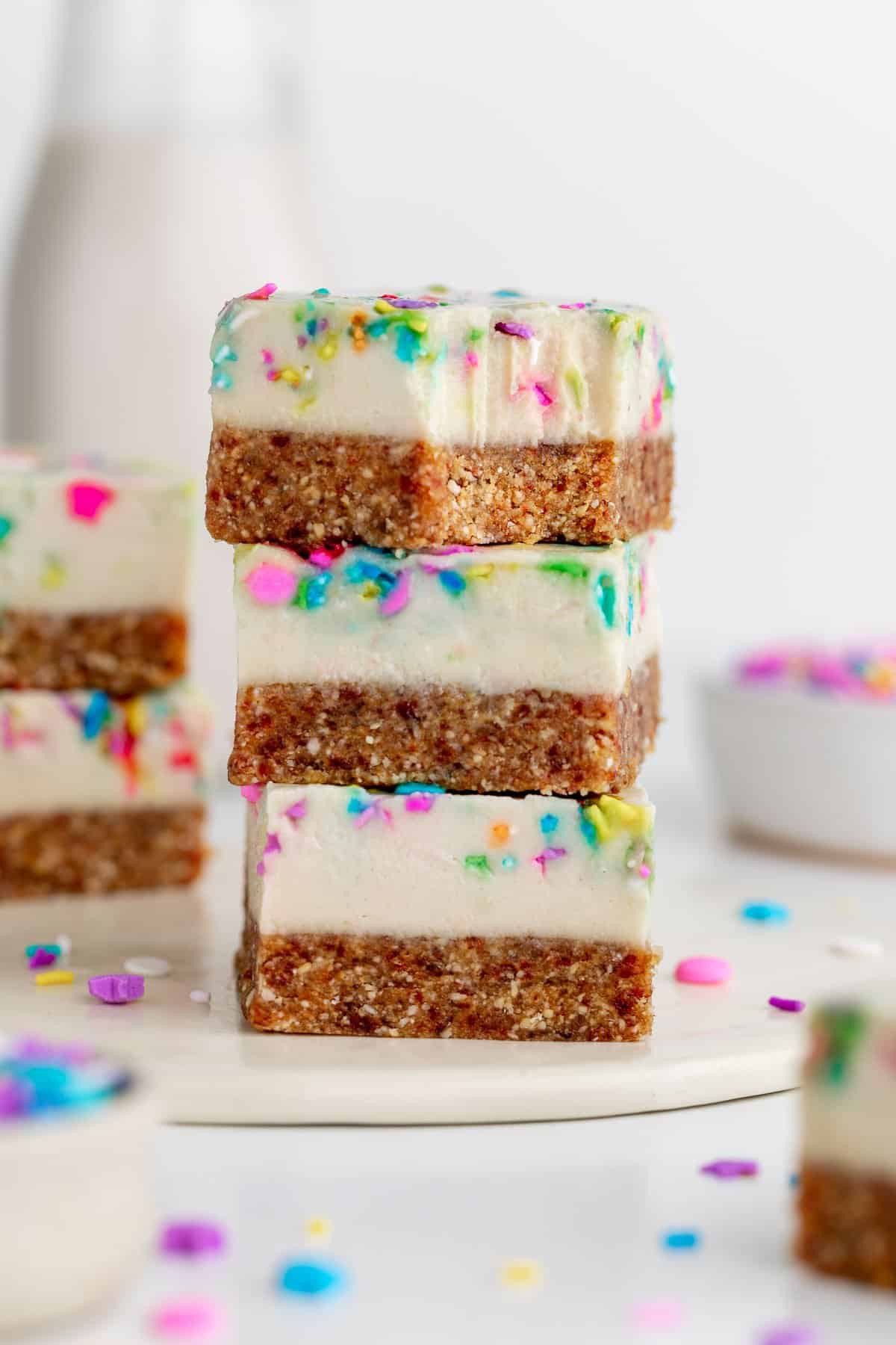 three no-bake funfetti cheesecake bars stacked with a bite taken out of the top one