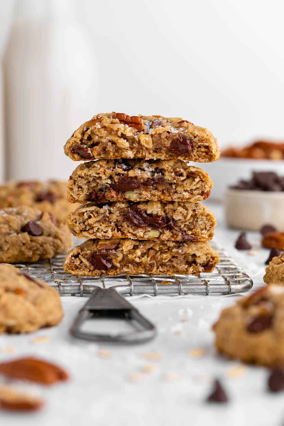 a stack of four vegan cowboy cookies sliced in half with gooey chocolate chips, oatmeal, pecans, and coconut