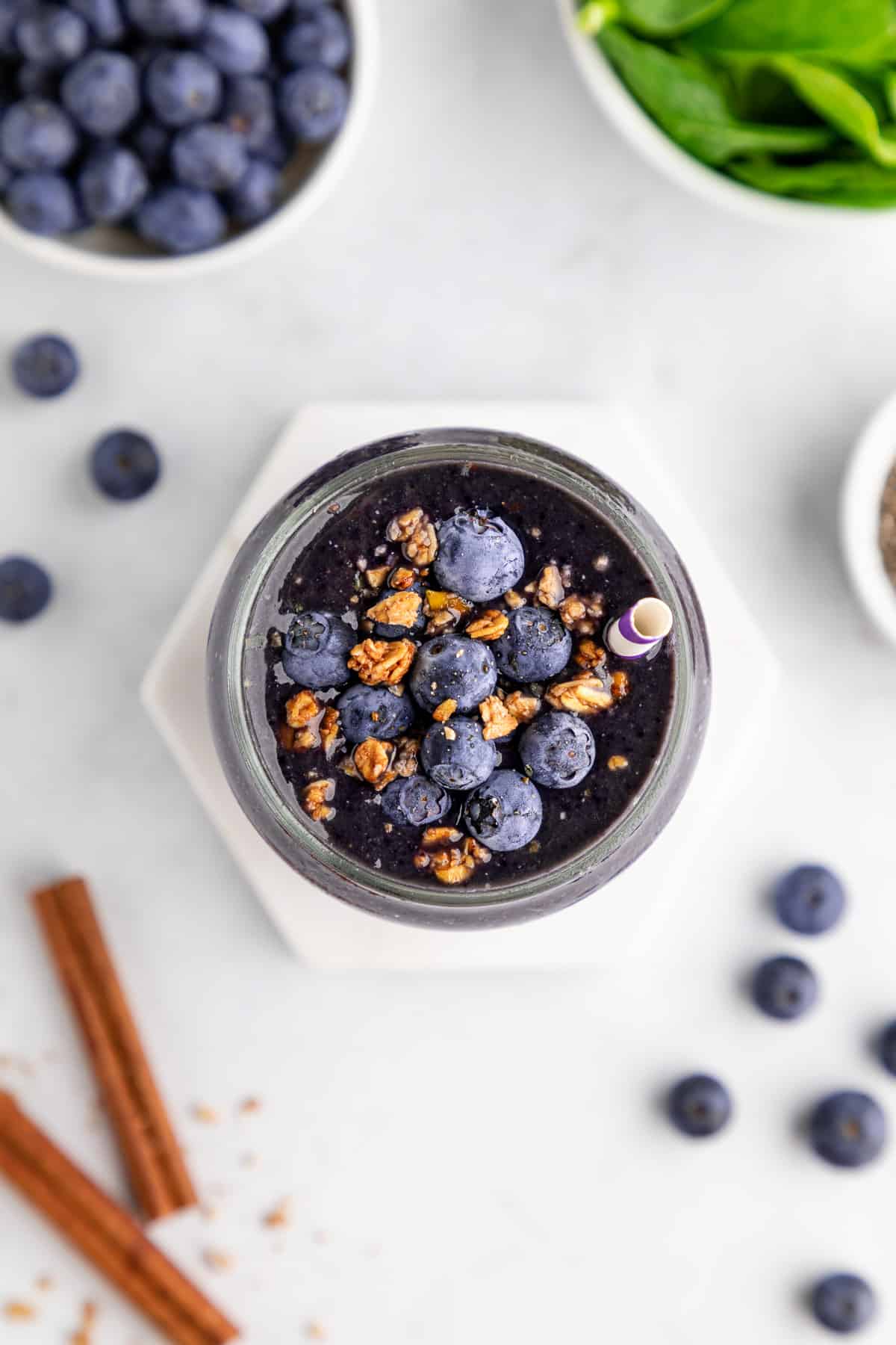 overhead photo of a blueberry spinach smoothie inside a glass with fresh blueberries and granola on top