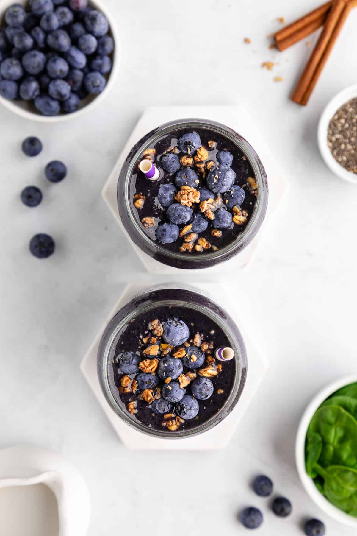 overhead photo of two glasses of blueberry spinach smoothie with granola on top