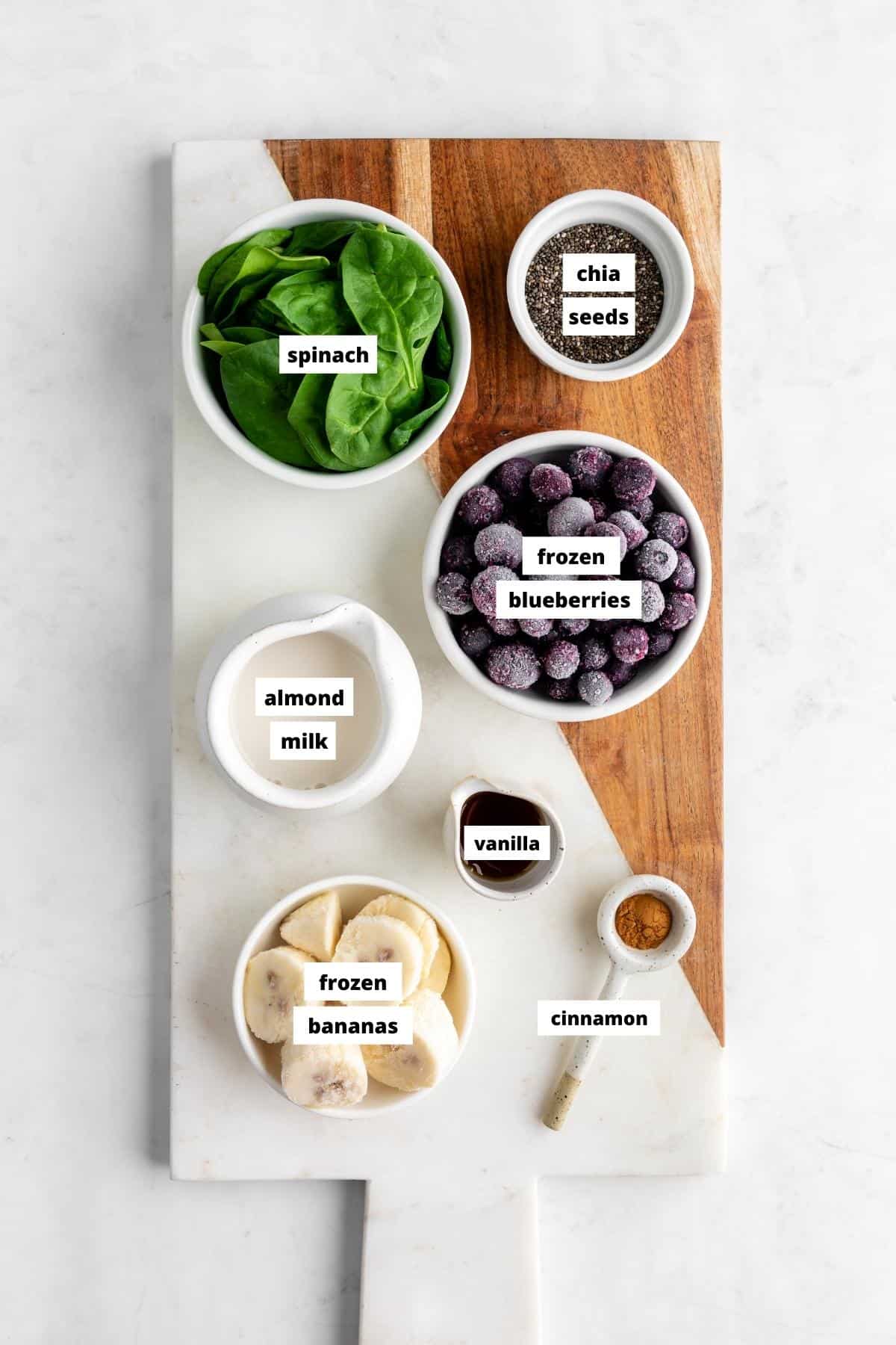 bowls of spinach, frozen blueberries, frozen bananas, almond milk, cinnamon, chia seeds, and vanilla on a marble serving board