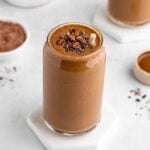 a chocolate banana smoothie inside a glass with cacao nibs on top