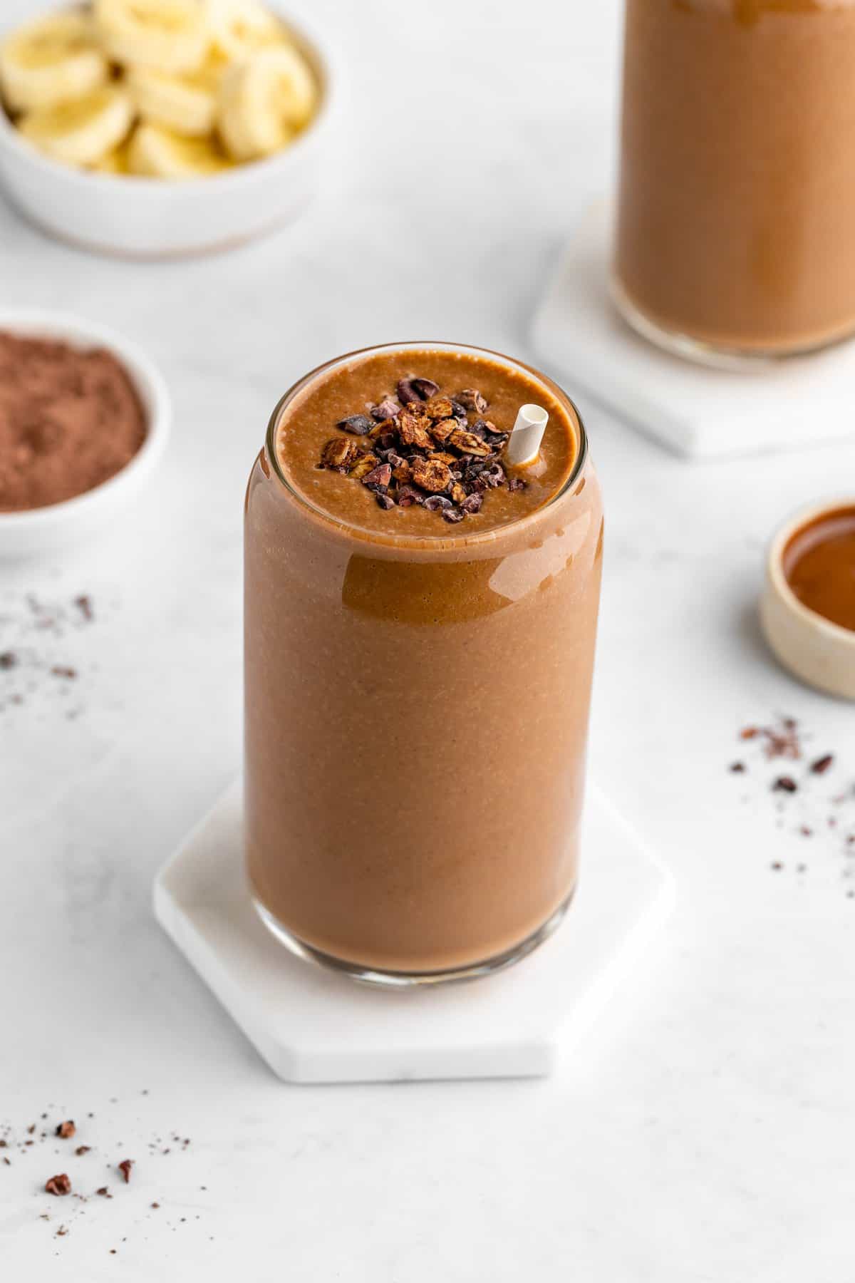 a chocolate banana smoothie inside a glass with cacao nibs on top