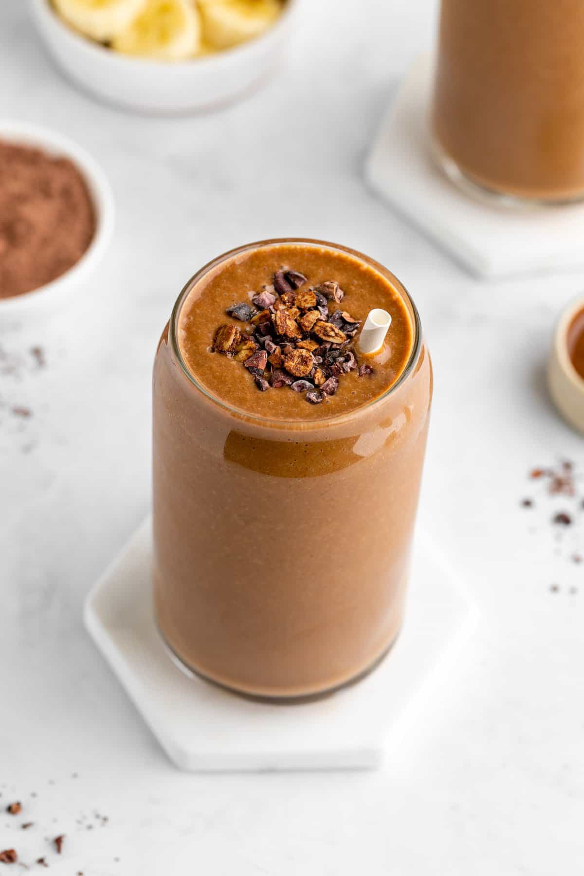 a chocolate banana smoothie inside a glass with cacao nibs and granola on top
