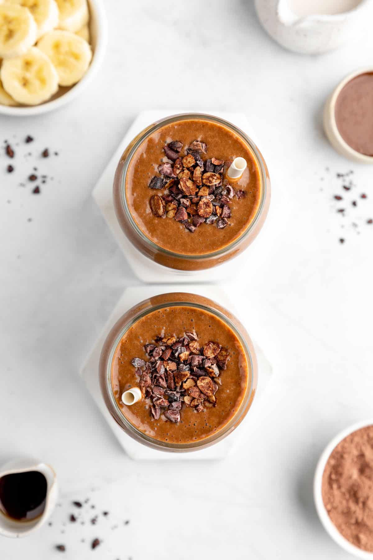 overhead image of two chocolate banana smoothies with cacao nibs on top