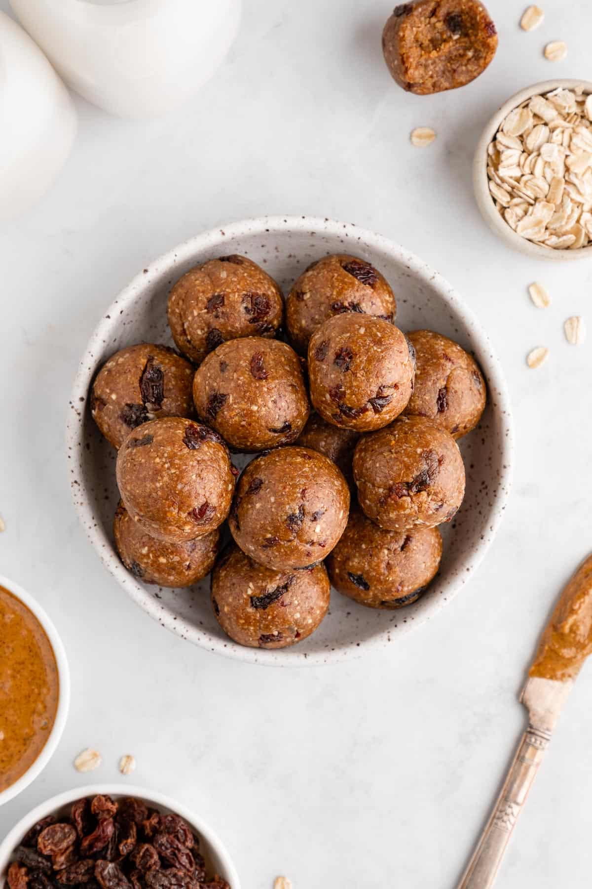 a bowl of oatmeal raisin energy bites surrounded with ingredients like rolled oats and almonds butter