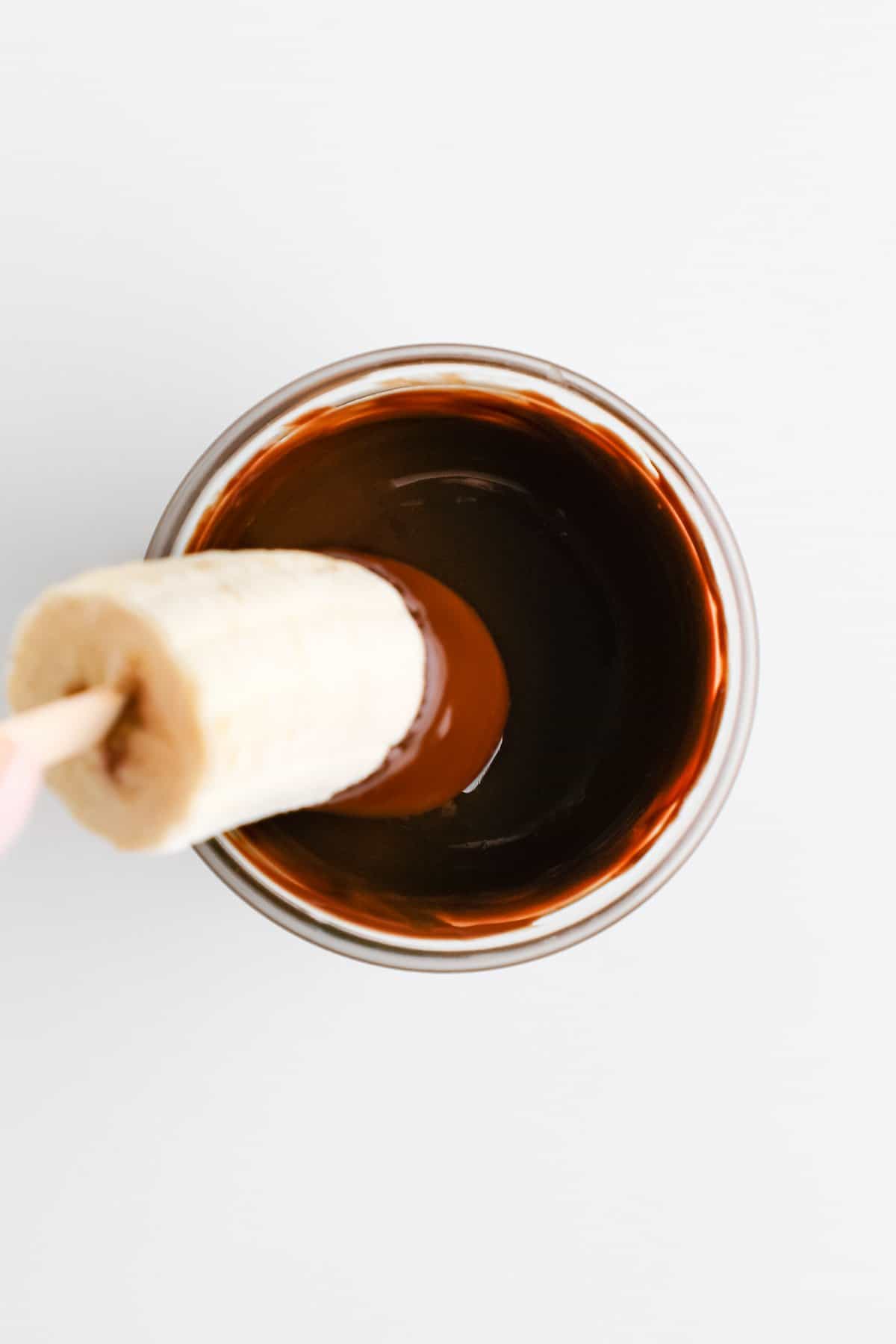 dipping a frozen banana pop into a weck jar filled with melted chocolate